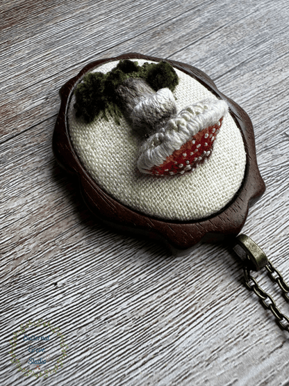 A tiny treasure from the forest floor, stitched by hand. Nestled inside a hand-carved walnut frame, this piece is small enough to wear as a pendant, or to add a bit of magic to your wall as a miniature work of art.  

Dimensions: 1.5" wide × 2" tall
Materials: Hand-stitched embroidery, hand-carved walnut frame

Choose how you would like to enjoy your little woodland treasure:

Please leave a note at checkout with your preference:

• Hand-painted mushroom picture hanger 
• 18" bronze chain with lobster clasp