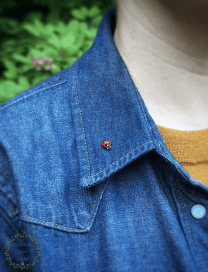A close-up of a person wearing a blue denim jacket over a mustard yellow sweater, with a small red ladybug pin attached near the collar.