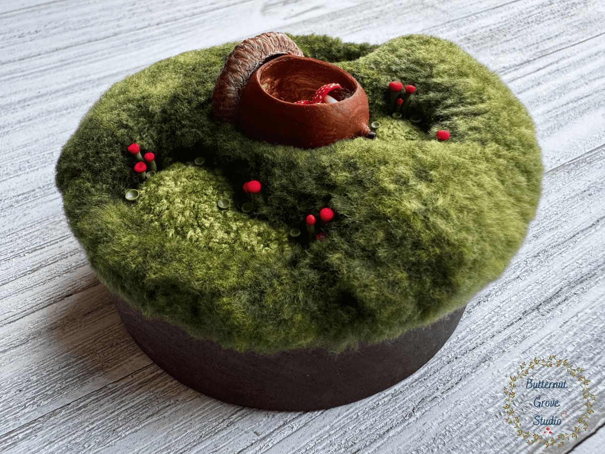 One-of-a-kind 3-inch micro-embroidery featuring a hand-carved acorn surrounded by embroidered moss, British soldier and fairy cup lichens, and tiny woodland details, framed in warm handmade walnut wood frame.